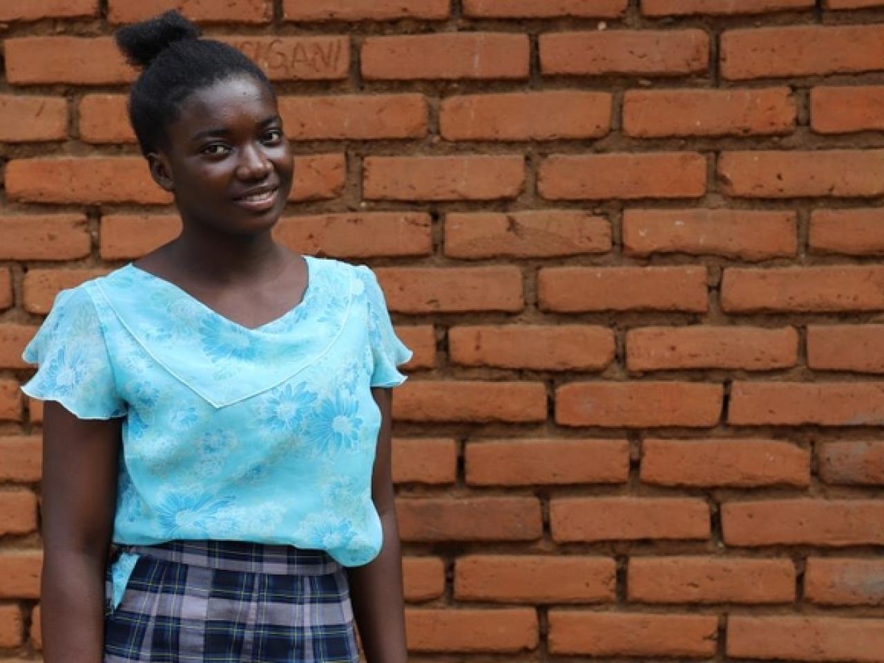 A girl in a blue shirt stands against brick background