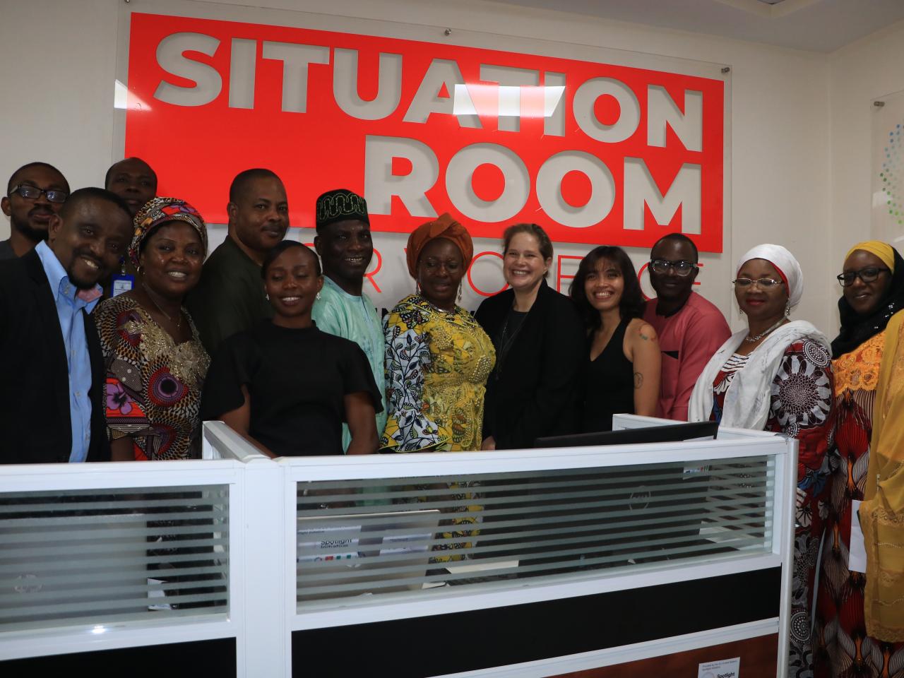 Men and women pose in front of situation room sign