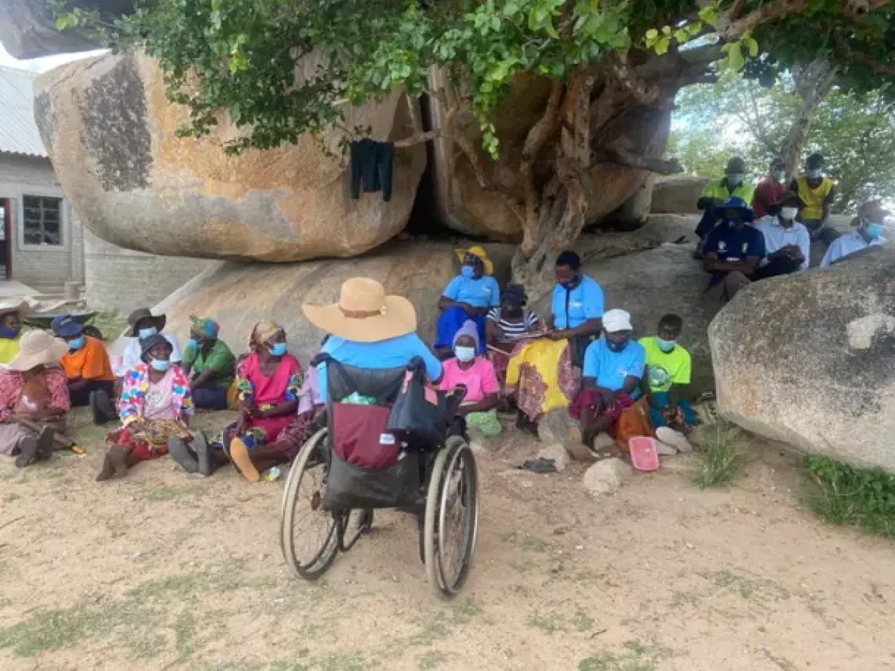 women sit under a tree while a woman in a wheelchair addresses them