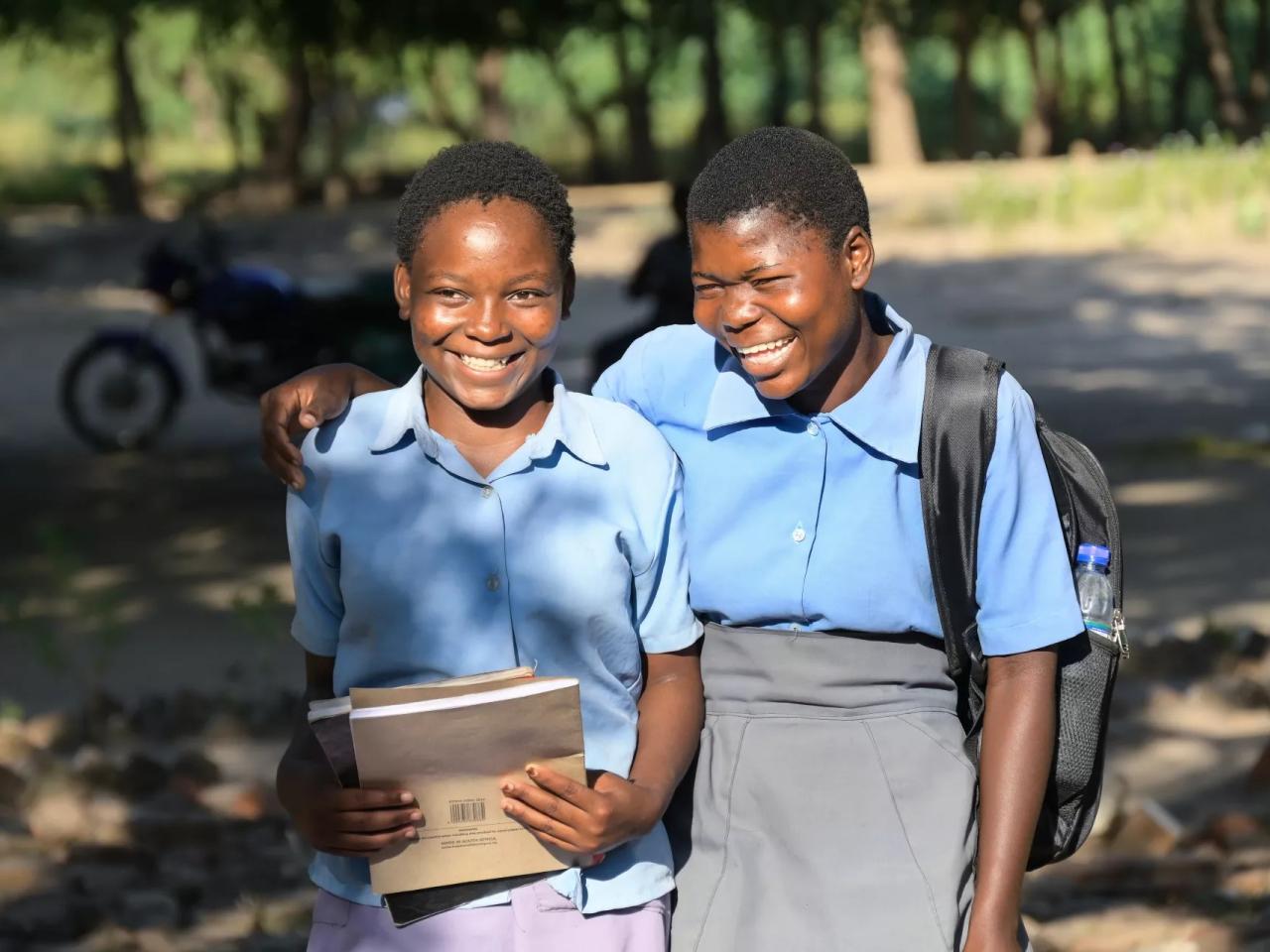 Two school girls walk with their arms around each others shoudlers