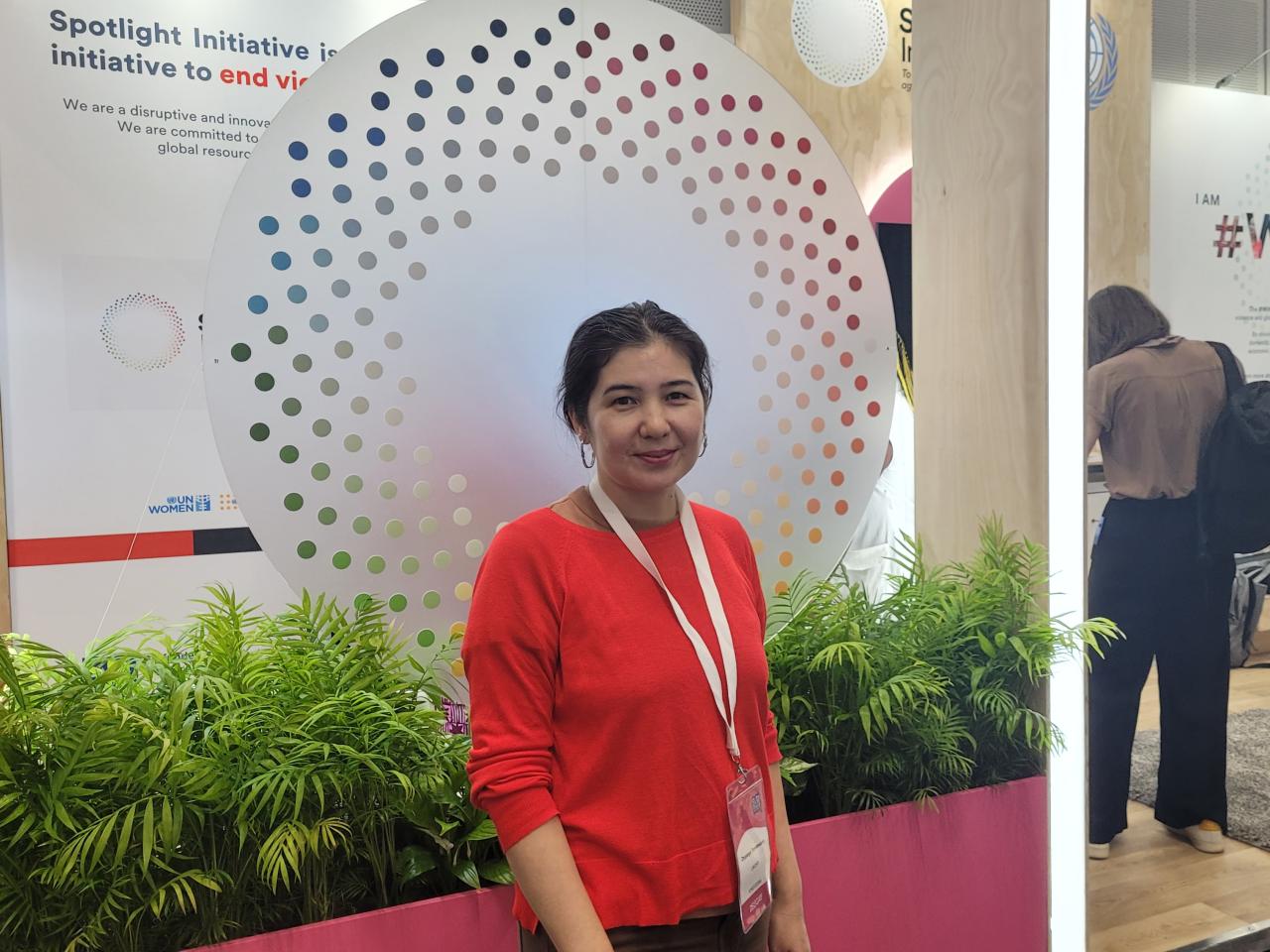 Woman in red shirt stands in front of Spotlight Initiative logo