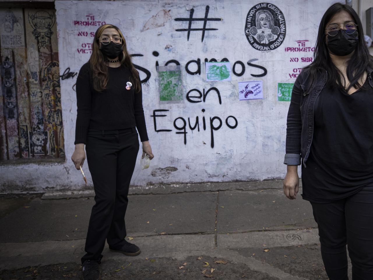 Two women stand in front of graffiti 