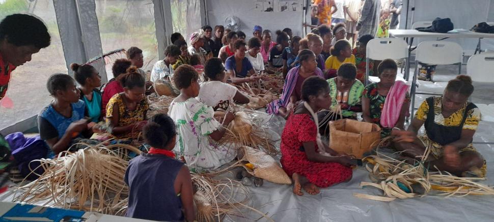 midwives are providing counsel on maternal health to visiting women, while the women are engaging also in income-generating activities, such as basket and mat weaving for selling.