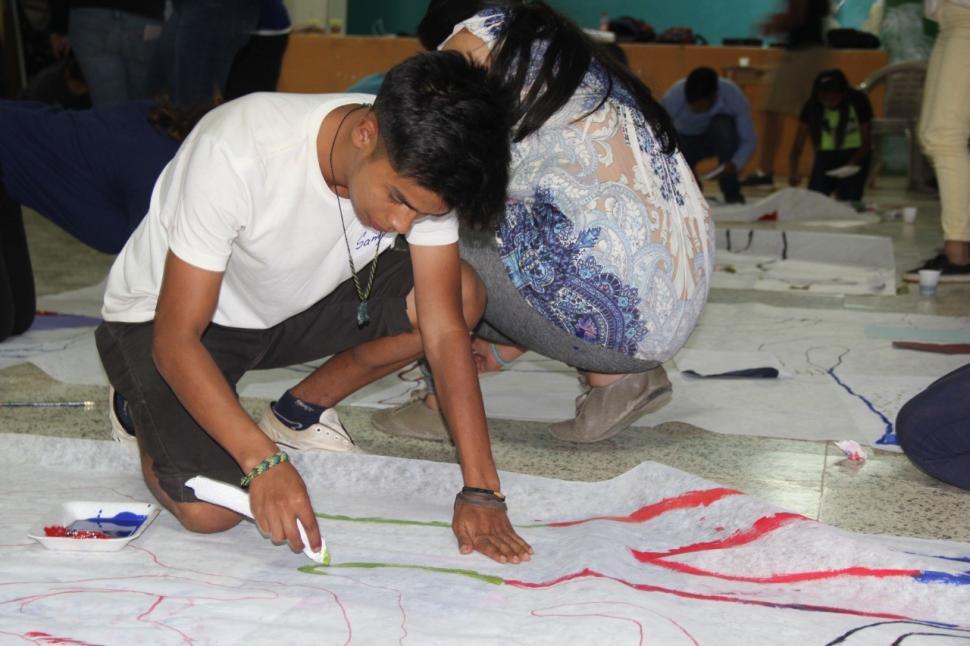 A boy applies paint to a large poster on the floor