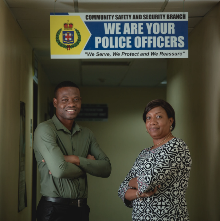 A man and a woman with folded arms stand under "we are your police officers" sign
