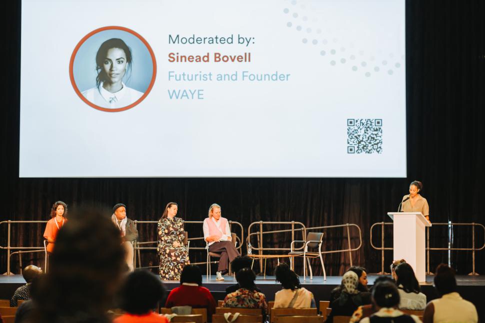 A woman speaking at lectern to audience and panellists