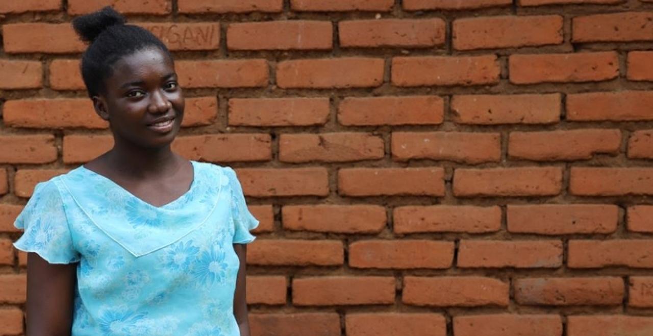 A girl in a blue shirt stands against brick background