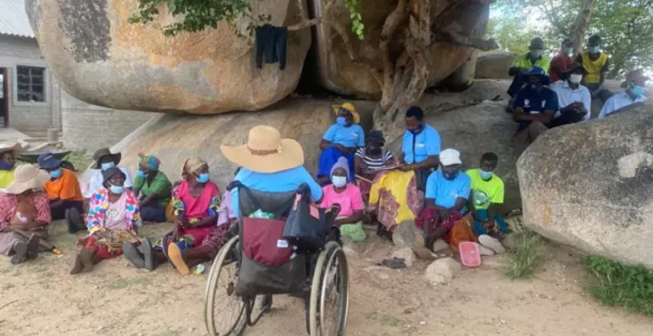women sit under a tree while a woman in a wheelchair addresses them