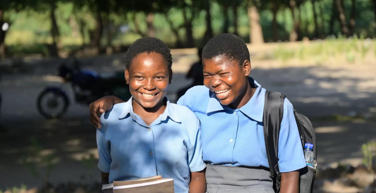 Two school girls walk with their arms around each others shoudlers