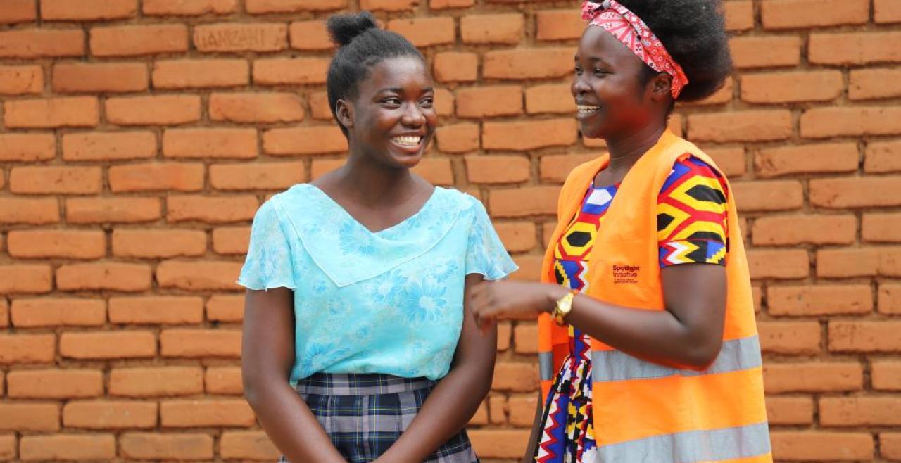 Two smiling girls chat, one wears an orange high visibility vest