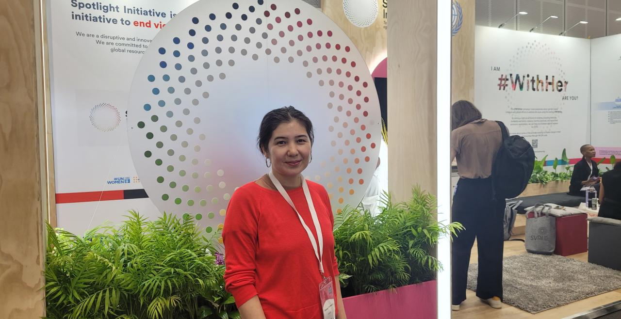 Woman in red shirt stands in front of Spotlight Initiative logo