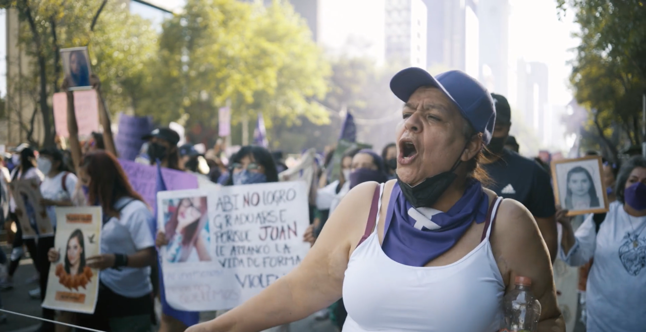A woman in purple hat and scarf shouts and leads a march