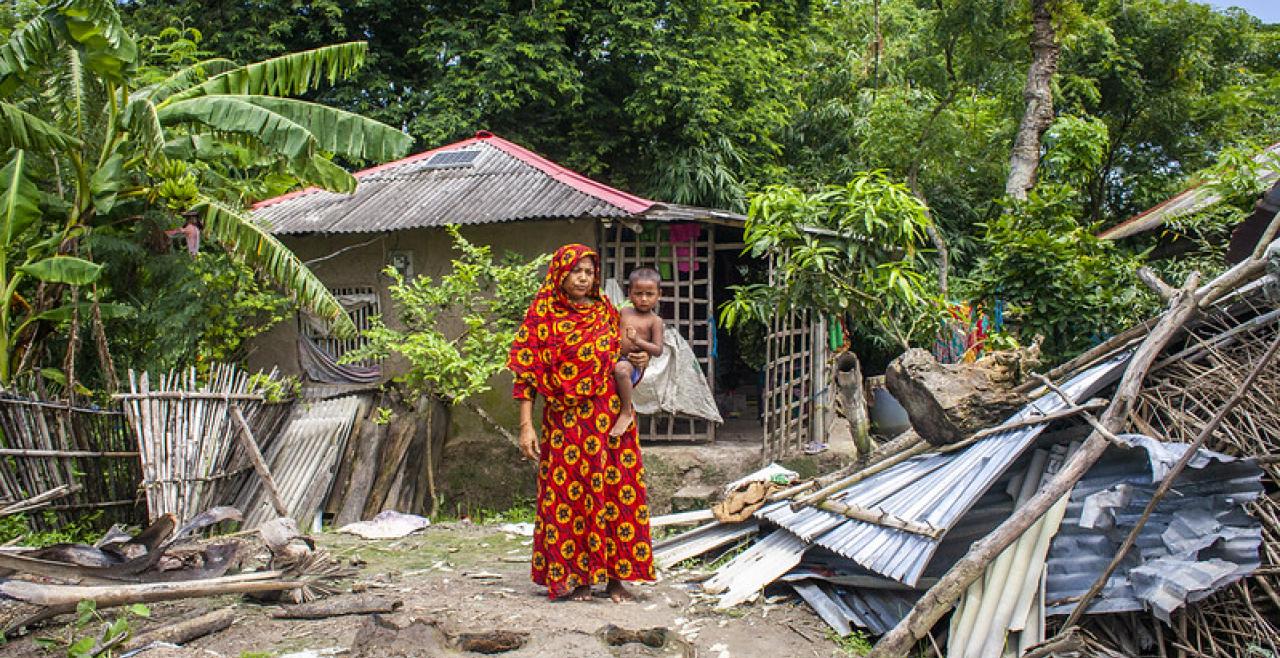 A woman holding a baby in front of a destroyed building