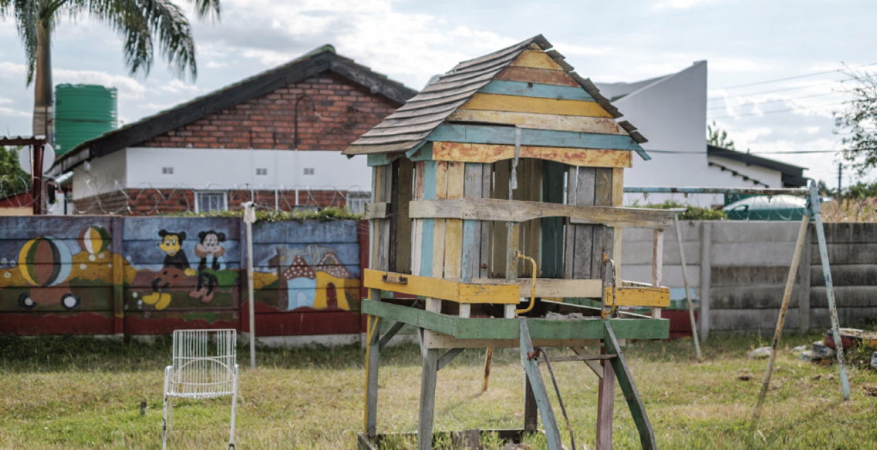 A children's playhouse stands in a grassy yard surrounded by a brightly painted fence